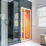 Remodeled bathroom in Great Falls, VA featuring a black marble walk-in shower with gold fixtures and an adjacent built-in infrared sauna.